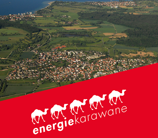 Luftbild einer Ortschaft; davor ein schräger roter Balken mit dem Logo der Energiekarawane