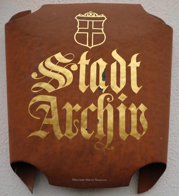 Auf einem rostbraunen Schild prangt ein goldener Schriftzug