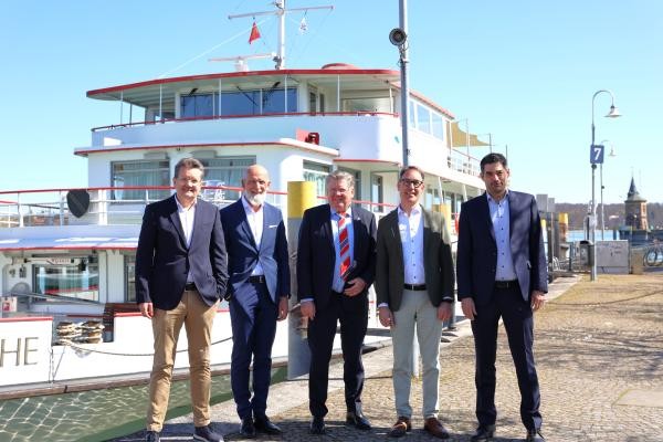 Fünf Männer stehen vor einem weißen Schiff.