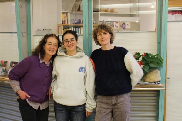 Drei Frauen stehen vor einer Wand mit drei Fenstern. Sie schauen lächelnd in die Kamera