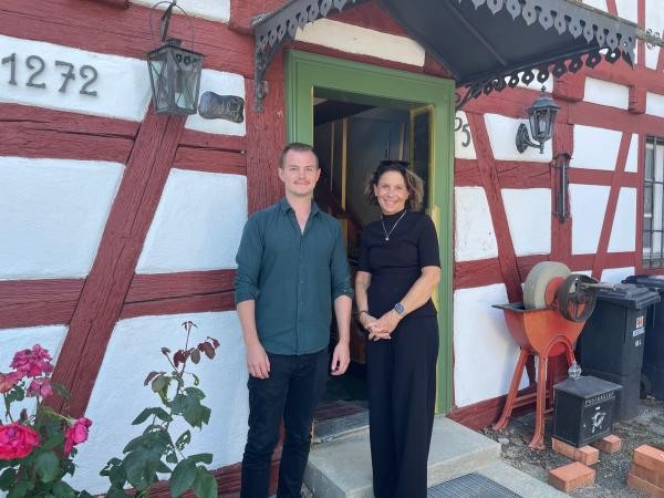 Ein junger Mann und eine Frau stehen vor einem überdachten Hauseingang zu einem Fachwerkhaus