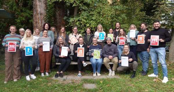 Copyright Stadt Konstanz Das Bild zeigt 22 Personen im Grünen, die teilweise stehen und teilweise sitzen, einige von ihnen halten Papiere mit Aufdrucken in den Händen