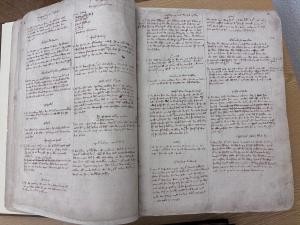 Ein historisches Buch liegt aufgeschlagen auf einem Tisch. Die Seiten sind vergilbt und sehr eng in Absätzen von Hand beschrieben.