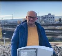 Pancho Westfeld von den Stadtwerken Konstanz hält lächelnd mit einer Straßenleuchte in der Hand vor der Europabrücke.