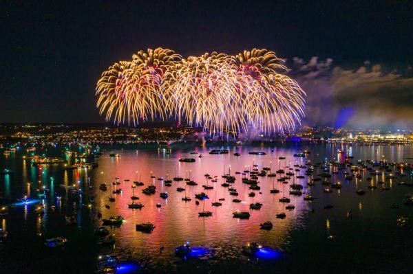 Boote auf einem See bei Nacht; im Hintergrund großes Feuerwerk