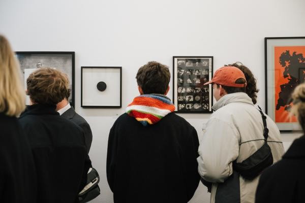 Mehrere Personen stehen mit dem Rücken zu Kamera vor einer Wand mit Werken von Jäger.