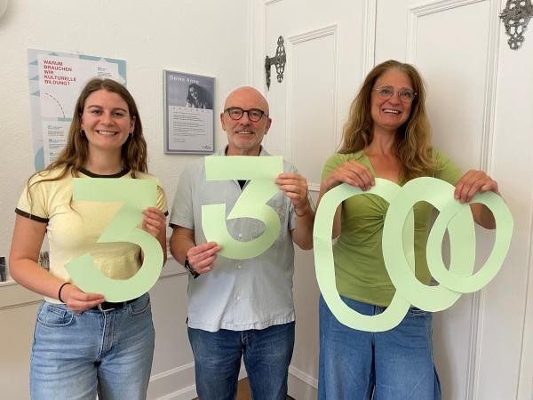 Drei Personen halten eine ausgeschnittene 33000 in die Kamera