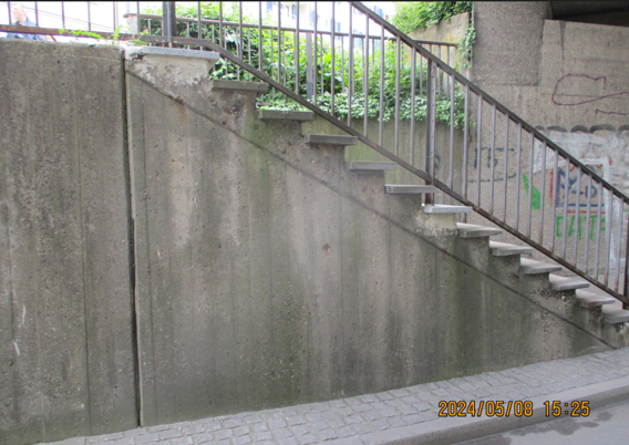Nicht barrierefreie Betontreppe am Sternenplatz in Konstanz mit Metallgeländer, die zu einem höhergelegenen Bereich führt. Die verwitterte Betonkonstruktion zeigt Moosansatz und Graffitispuren, im Hintergrund ist Grünbewuchs sichtbar.