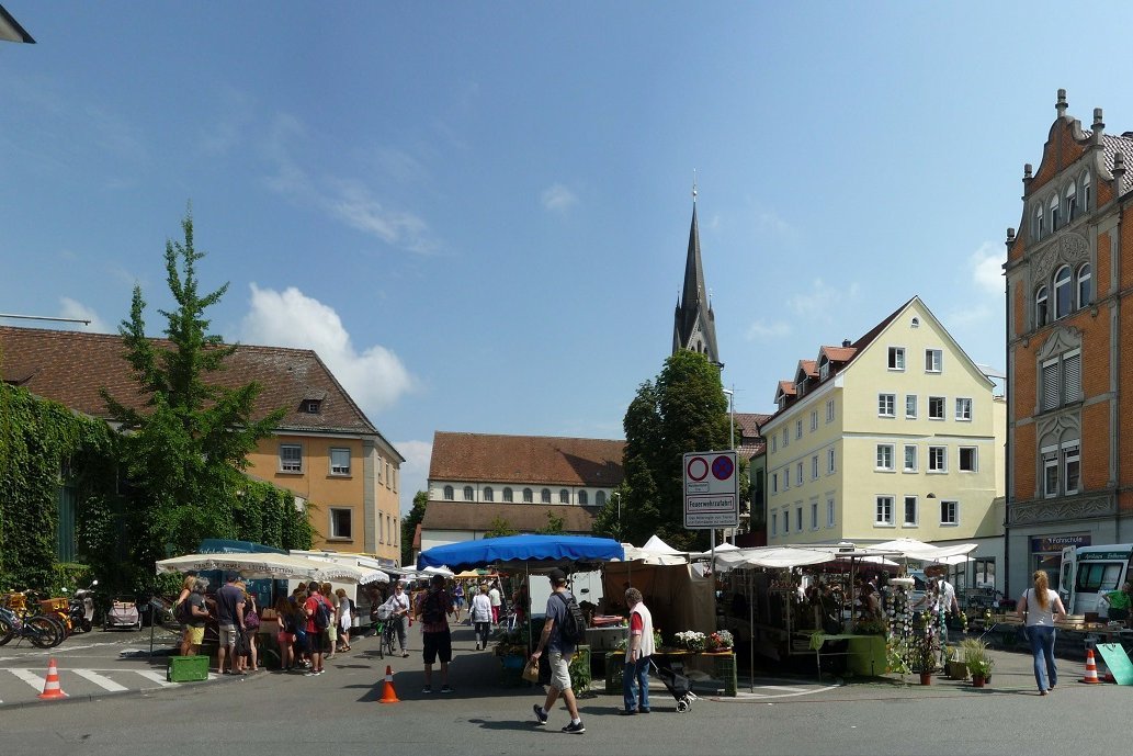 Blick auf einen mit Häusern umstellten Platz, auf dem ein Wochenmarkt stattfindet