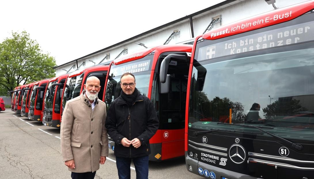 Zwei Herren im Außenbereich vor in der Reihe nebeneinander geparkten roten Bussen