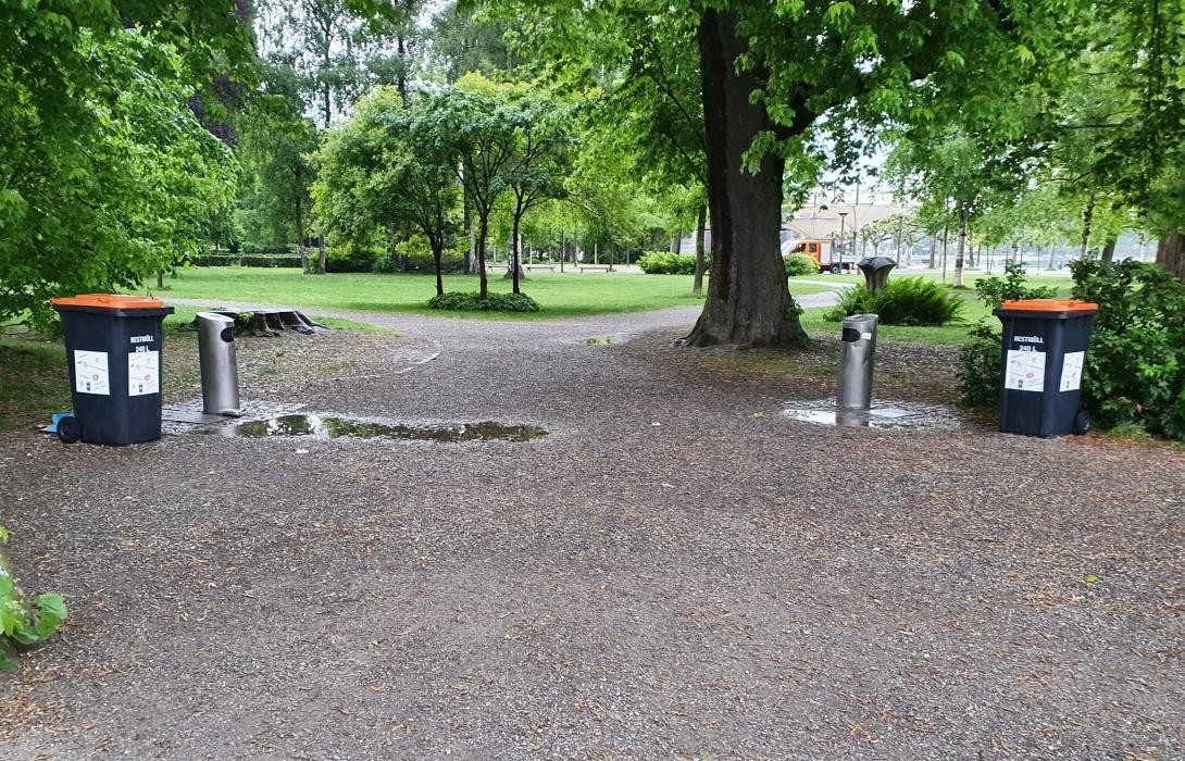 Blick in einen Park mit öffentlichen Mülleimern am Rand des Wegs