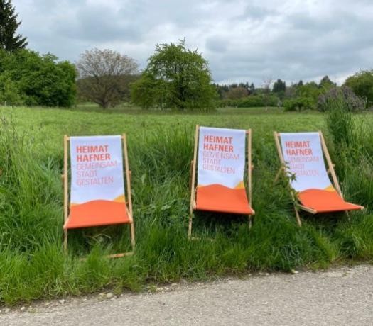 Drei Liegestühle mit orangenem Hafner-Logo stehen am Wegesrand auf einer grünen Wiese