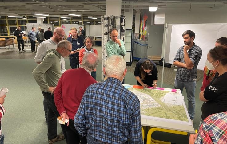 Ein Grüppchen Menschen steht um einen Tisch, auf dem ein Stadtplan ausliegt