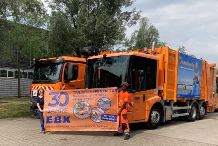 Zwei Personen halten den Banner von der EBK vor zwei Müllfahrzeugen hoch