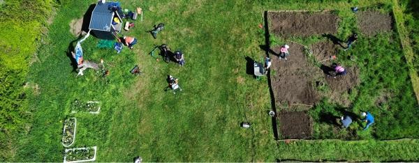 Schulgarten aus der Vogelperspektive: Grüne Wiese, Beete, bepflanzte Badewannen und eine Gartenhütte