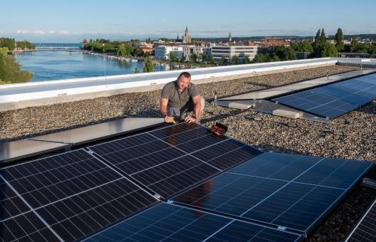 Mann auf einem Dach, während er Photovoltaik-Module installiert