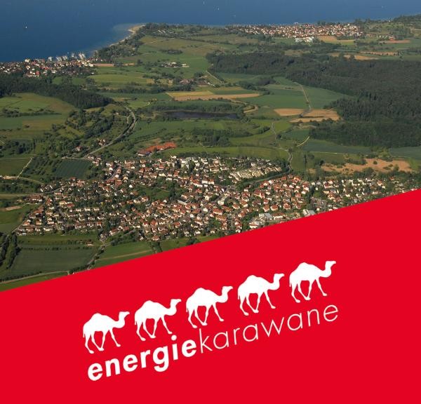 Luftbild einer Ortschaft; davor ein schräger roter Balken mit dem Logo der Energiekarawane