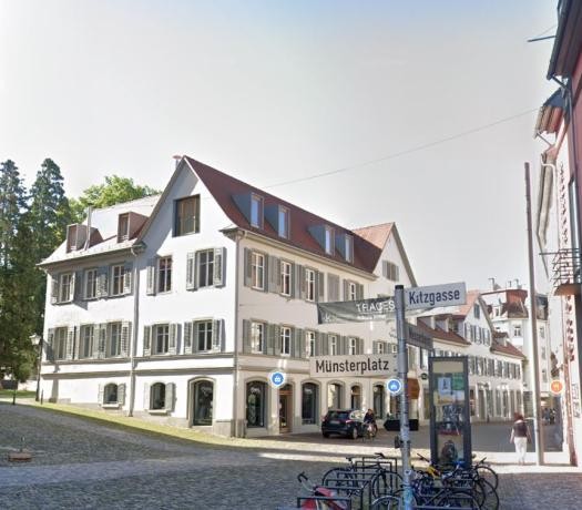 Straßenflucht mit Blick auf ein weißes Eckhaus mit rotem Dach und grünen Fensterläden
