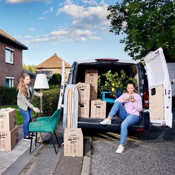 Umzugssitzution im beladenem Transporter, Frau mit Handy in der Handy