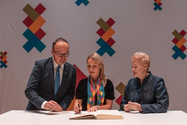 Ein Mann und zwei Frauen an einem Tisch. Eine Frau schreib in ein Buch.