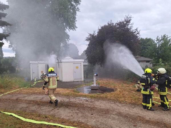 Feuerwehrleute spritzen bei Übung Wasser mit dem Schlauch auf rauchendes Gebäude