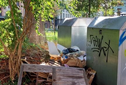 Müllberg hinter Glascontainern, darunter Tisch und Stühle.