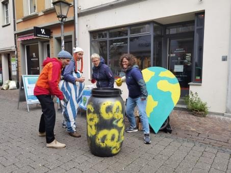 Vier Personen stehen um eine schwarze Plastiktonne herum. Sie tragen jeweils einen Boxhandschuh, mit dem sie auf die Tonne zielen.