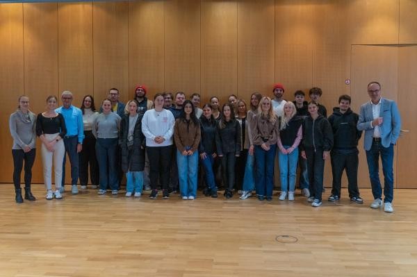 Viele Menschen stehen in einer Reihe vor einer holzvertäfelten Wand.