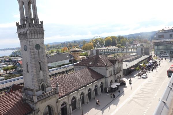 Von oben zu sehen das Bahnhofsgebäude sowie eine breite grau asphaltierte Straße auf der Konstanz eingefräst wurde.