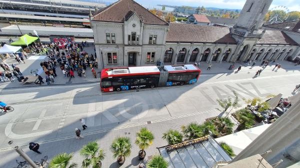Zu sehen ist der neu gestaltete Bahnhofplatz von oben, sowie Teile des Bahnhofgebäudes und ein roter Stadtbus. Zudem befinden sich viele Personen auf dem Bild.