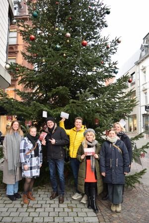 Eine Gruppe von Menschen steht vor einem hohen, geschmückten Weihnachtsbaum in der Konstanzer Fußgängerzone.
