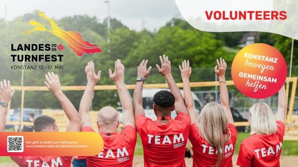 Mehrere Personen in roten T-Shirts mit der Aufschrift „TEAM“ stehen nebeneinander und heben gemeinsam die Arme in die Luft. Im Hintergrund ist ein Volleyballfeld zu sehen. Links oben das Logo des Landesturnfestes 2026 mit Datum und Ort „Konstanz 13.–17. Mai“. Rechts oben steht „VOLUNTEERS“. Ein runder Farbverlauf enthält den Slogan „Konstanz bewegen – gemeinsam helfen“. Unten links befindet sich ein QR-Code mit dem Hinweis auf das Helferportal und der Webadresse