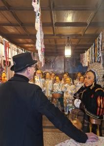 Mehrere Verkleidete in traditionellen weißen Häs und bunten Bändern stehen in einer festlich geschmückten Halle. Im Vordergrund sind eine Person im schwarzen Anzug und ein Hansele mit kunstvoller Kopfbedeckung zu sehen. Die Stimmung ist feierlich.