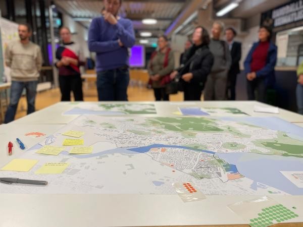 Karte und Klebenotizzettel auf einem Tisch; im Hintergrund verschwommen eine Gruppe Menschen