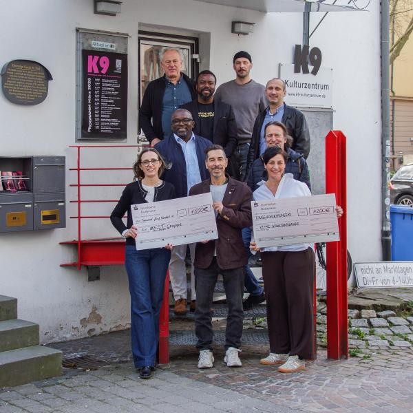 Das Bild zeigt neun Personen, die gestaffelt in 4 Reihen verteilt auf einer Treppe stehen, die vordere Reihe hält Spendenchecks in den Händen