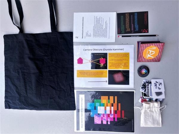 Ein schwarzer Jutebeutel und daneben liegen verschiedene Flyer und Infoblätter, Aufkleber und Bleiistift