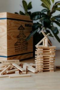 Ein Turm aus Holzklötzen, im Hintergrund eine hohe Holzkiste und eine dunkelgrüne Zimmerpflanze.