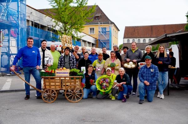 Eine Gruppe Marktbeschicker mit einem Bollerwagen. Sie halten Lebensmittel und Blumen in den Händen.