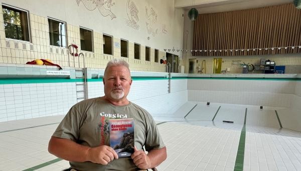 Ein Mann hält ein Buch, während er in einem leeren Schwimmbecken sitzt.