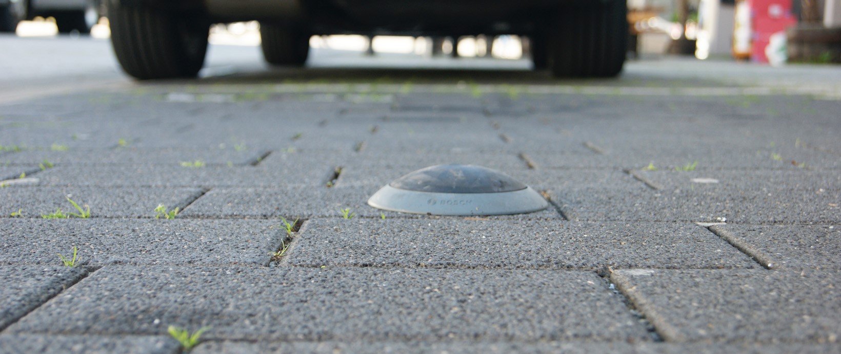 Parkraumsensor auf Pflastersteinen, im Hintergrund ein Auto