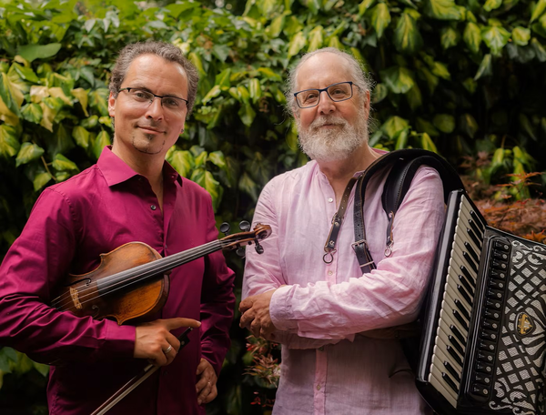 Das Bild zeigt die beiden Musiker Dr. Alan Bern und Mark Kovnatskiy mit ihren Instrumenten, einer Violine und einem Akkordeon.