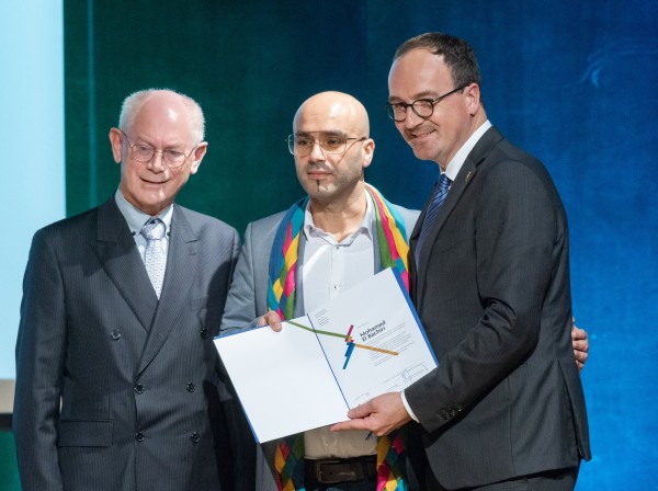 Drei Personen stehen nebeneinander mit einer aufgeschlagenen Mappe in der Hand