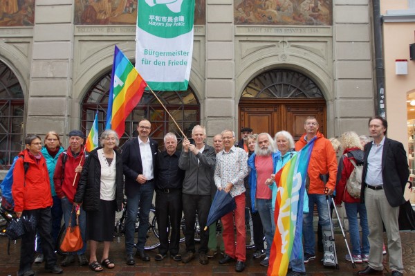Eine große personengruppe mit Regenbogenflagge stehen vor einer historischen Hausfassade