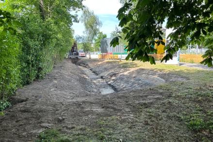 Blick auf den frisch ausgehobenen Graben. Im Hintergrund ist ein Bagger.