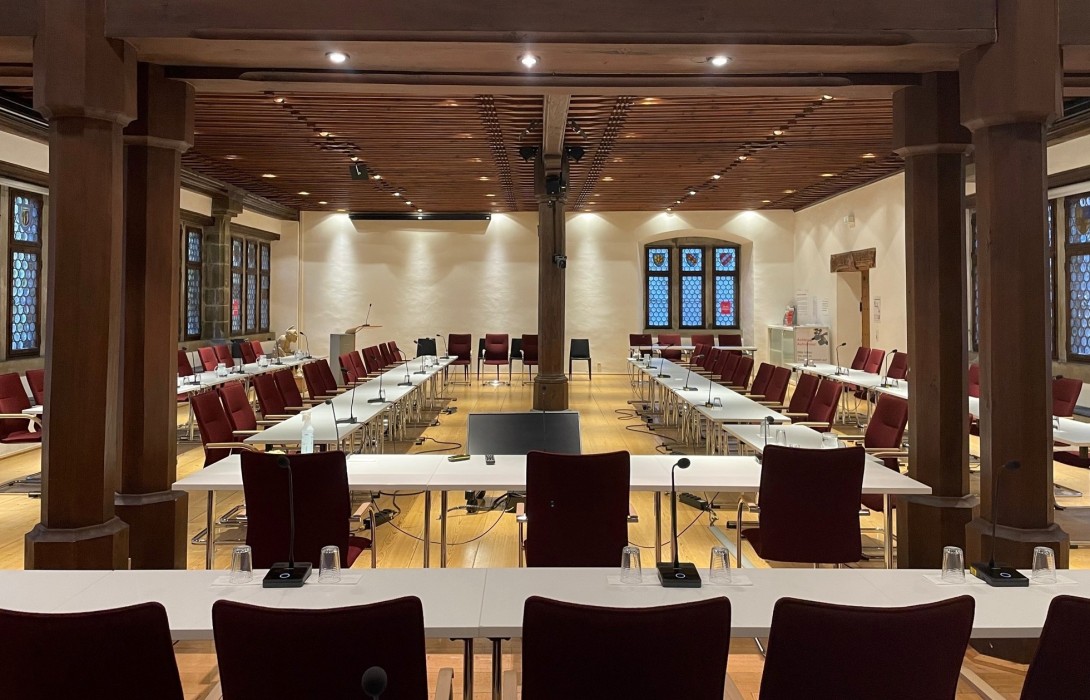 Blick in den Konstanzer Ratssaal mit im Rechteck aufgestellten Tischen und roten Stühlen