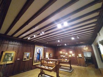 Blick in einen Ausstellungsraum mit Holz-verkleideten Wänden, Bildern an den Wänden und Ausstellungstischen in der Mitte