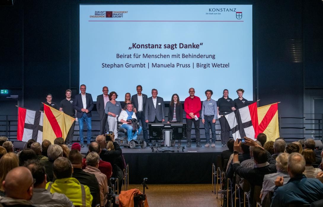 Ein Gruppe menschen steht vor eine Leinwand, auf der folgender Text projeziert ist: "Konstanz sagt Danke. Beirat für Menschen mit Behinderung. Stephan Grumbt, Manuela Pruss, Birgit Wetzel."
