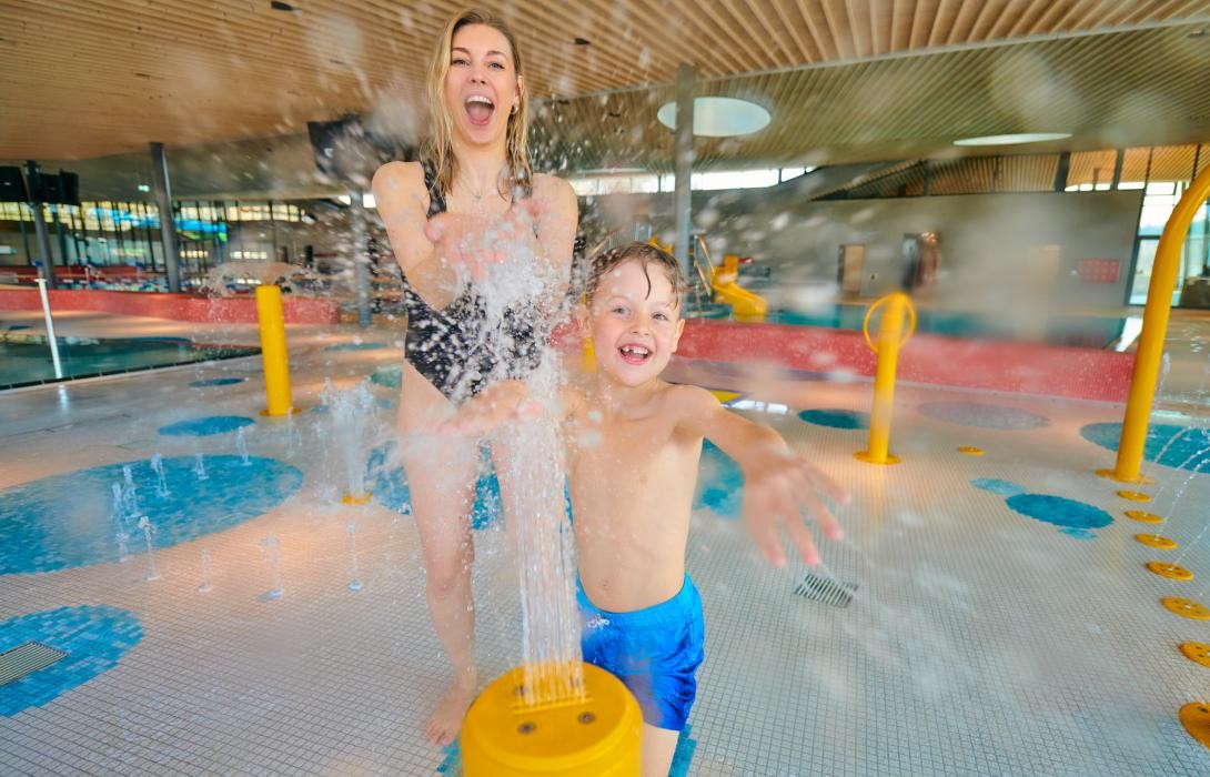 Eine Frau und ein Kind spielen an einer Wasserfontaine.