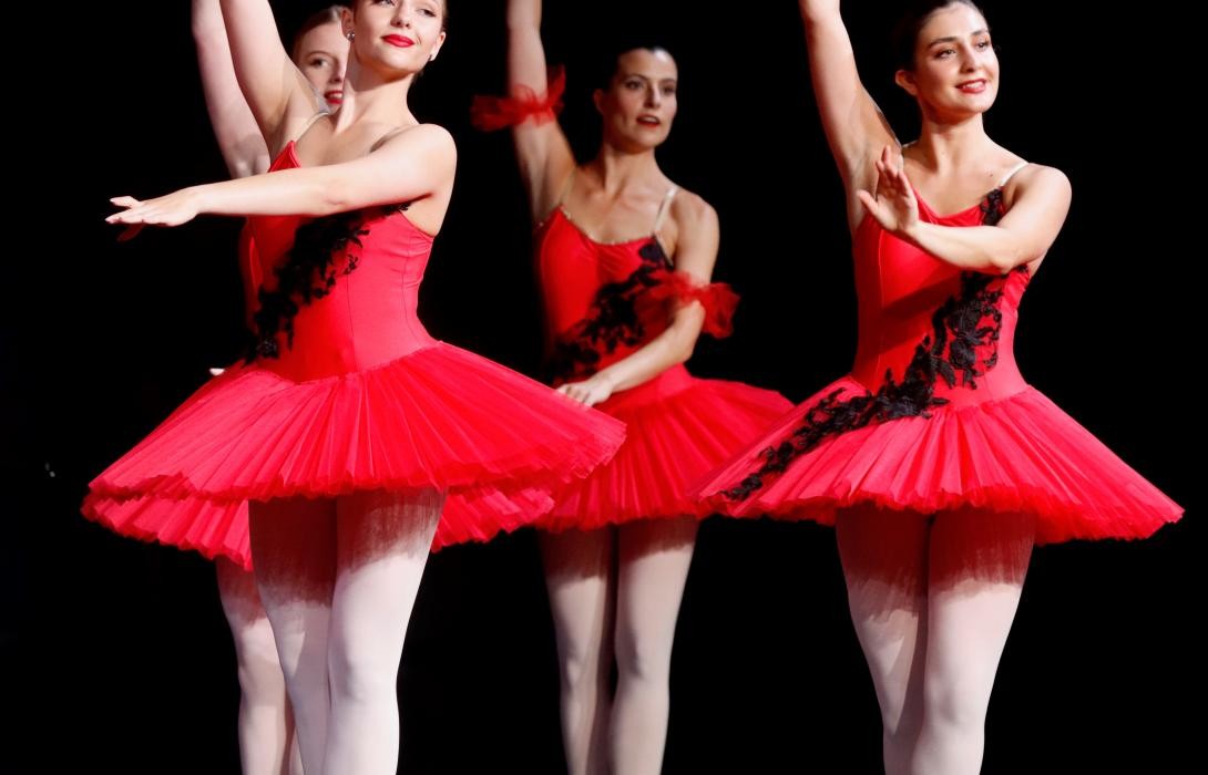Drei Ballerinas in roten Kleidern vor schwarzem Hintergrund.