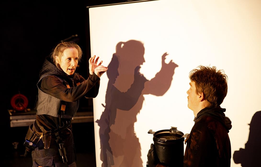 Zwei Personen vor einer Leinwand schauen sich, eine formt Schattenfiguren mit ihren Händen.